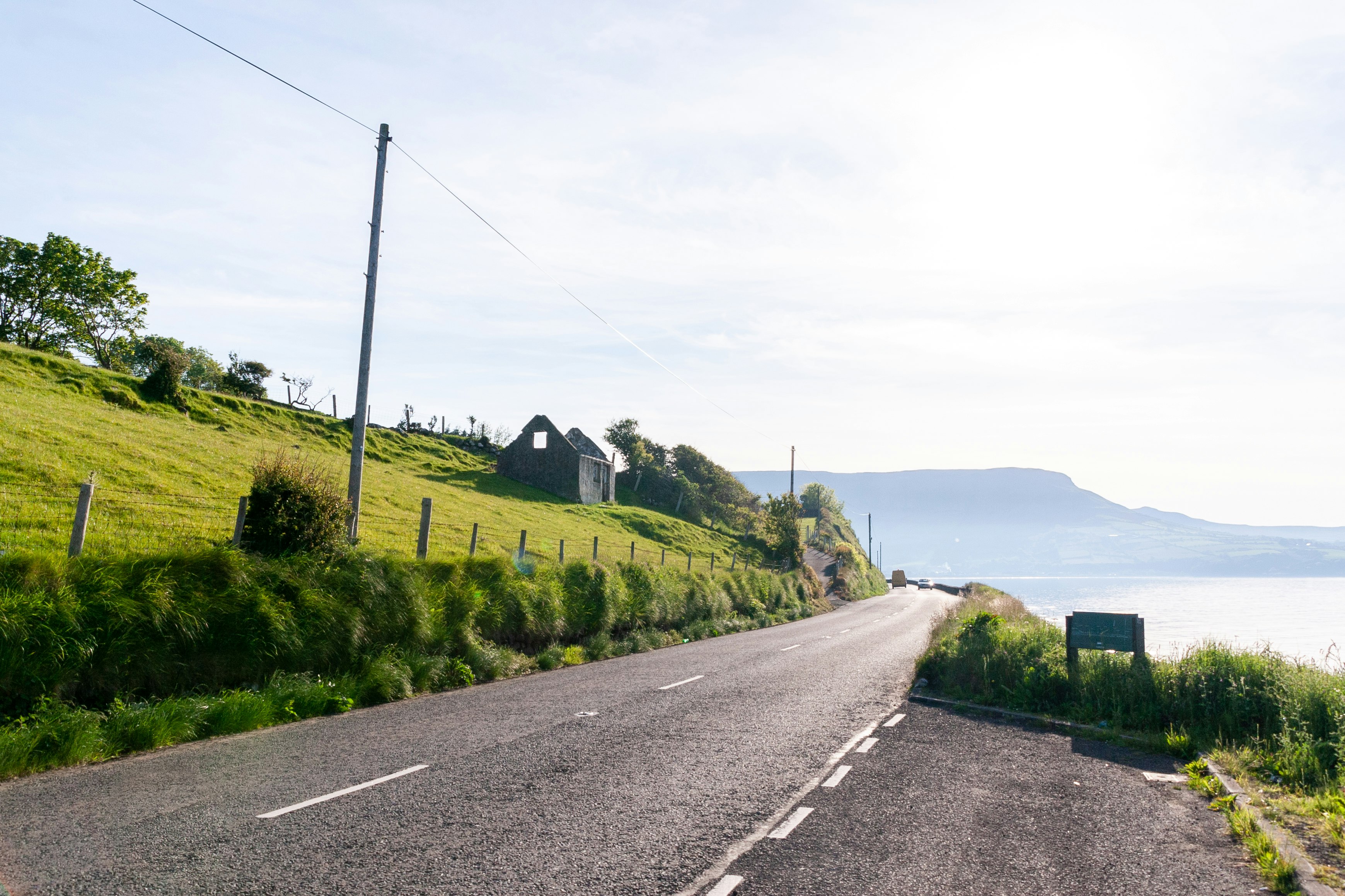 gray asphalt road between green grass field under white sky during daytime